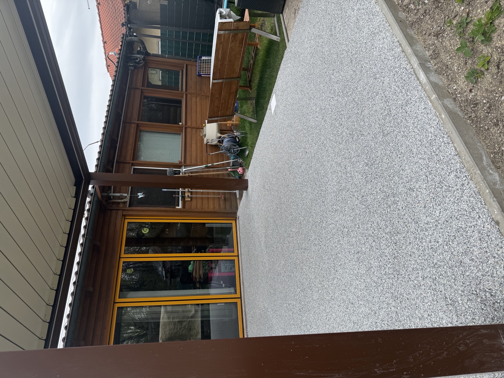Außenbereich mit Natursteinteppich in Grau vor Holzhütte und Gartenhaus