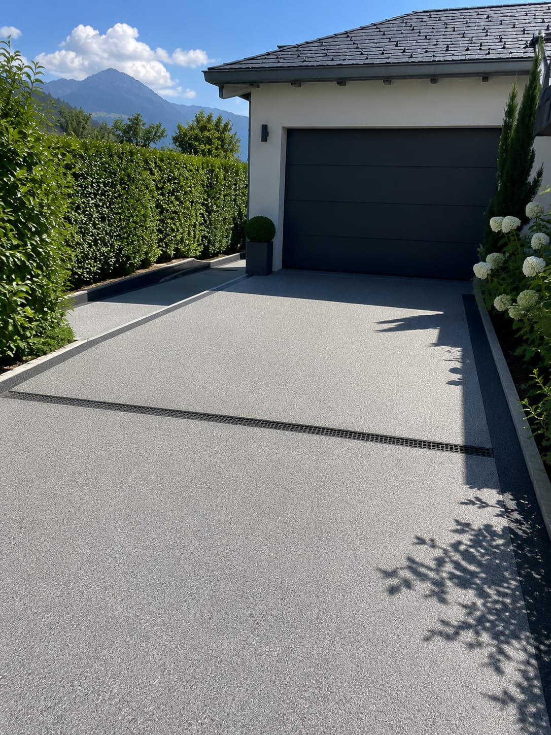 Natursteinteppich-Einfahrt in Grau vor Garage mit Entwässerungsrinne und Bergblick