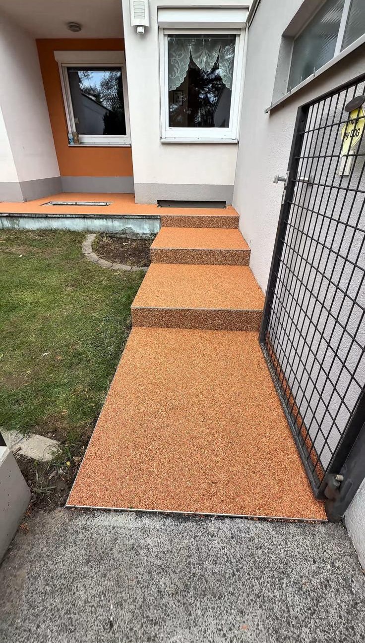 Eingangstreppe und Vorbereich mit Natursteinteppich in warmem Terracotta-Orange