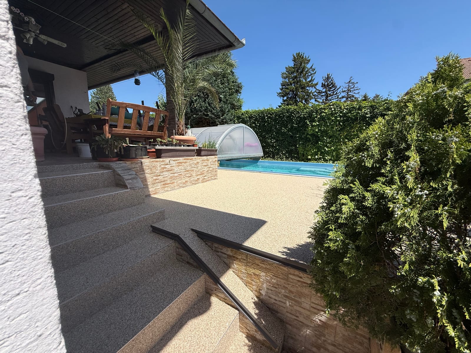 Natursteinteppich-Poolterrasse in Beige mit Stufen und Handlauf vor überdachtem Sitzbereich