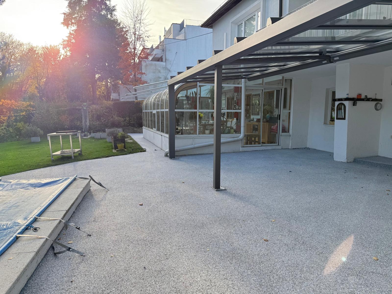 Hellgrauer Natursteinteppich auf großer Terrasse mit Wintergarten und Gartenblick